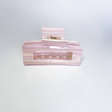 A pearlescent, light pink hair claw clip with a visible metal spring is shown head-on against a white background.